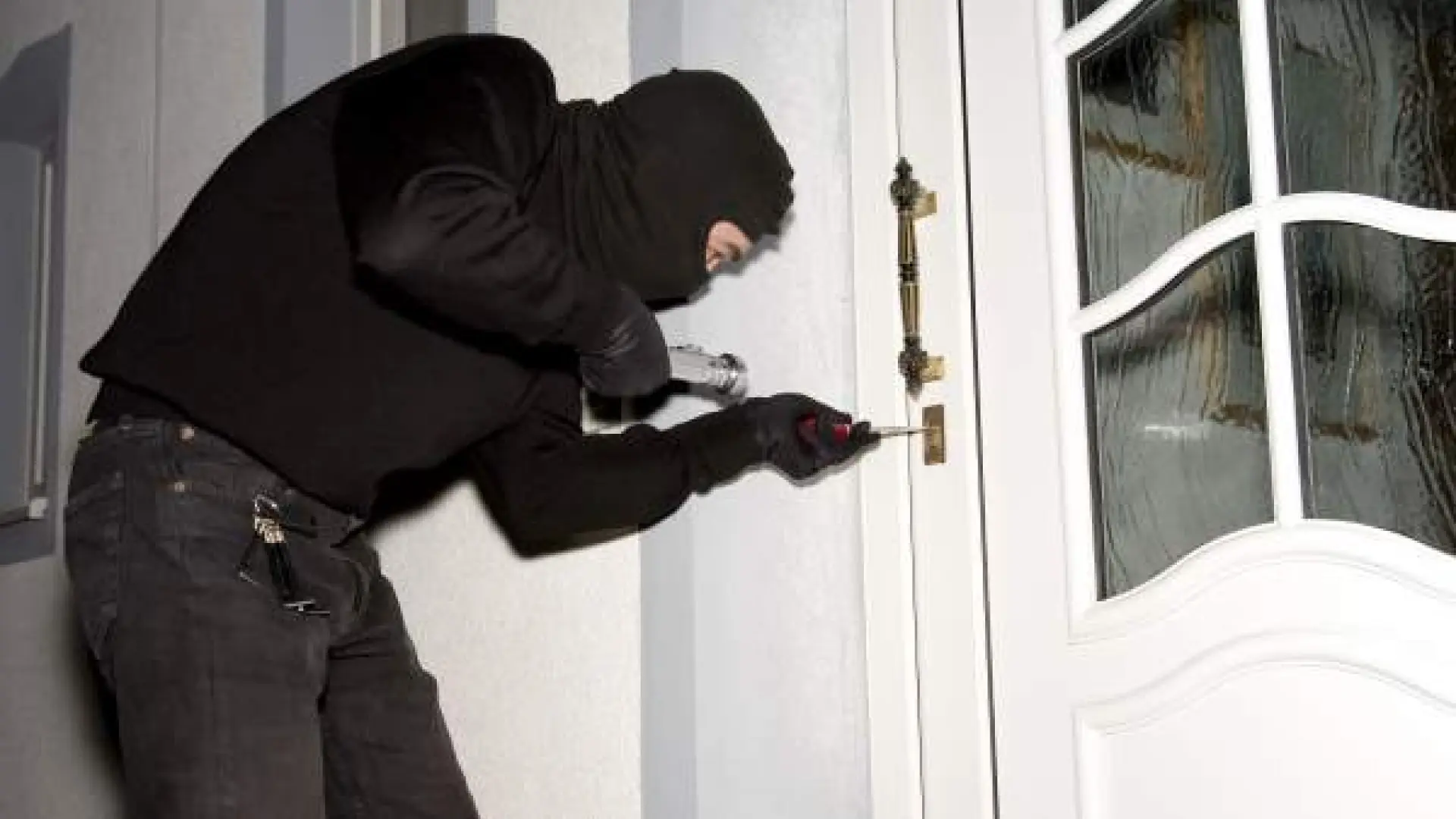 Persona intentando forzar la puerta de una vivienda, imagen relacionada con la prevención de robos durante las vacaciones.