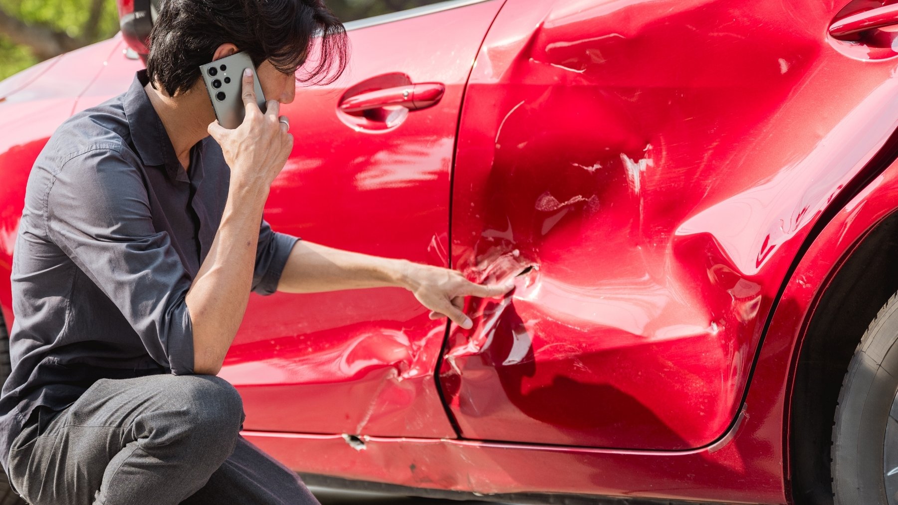 Accidente con un coche que no es tuyo Persona hablando por teléfono junto a un coche accidentado, imagen relacionada con un accidente de tráfico ocurrido con un vehículo que no es de su propiedad.